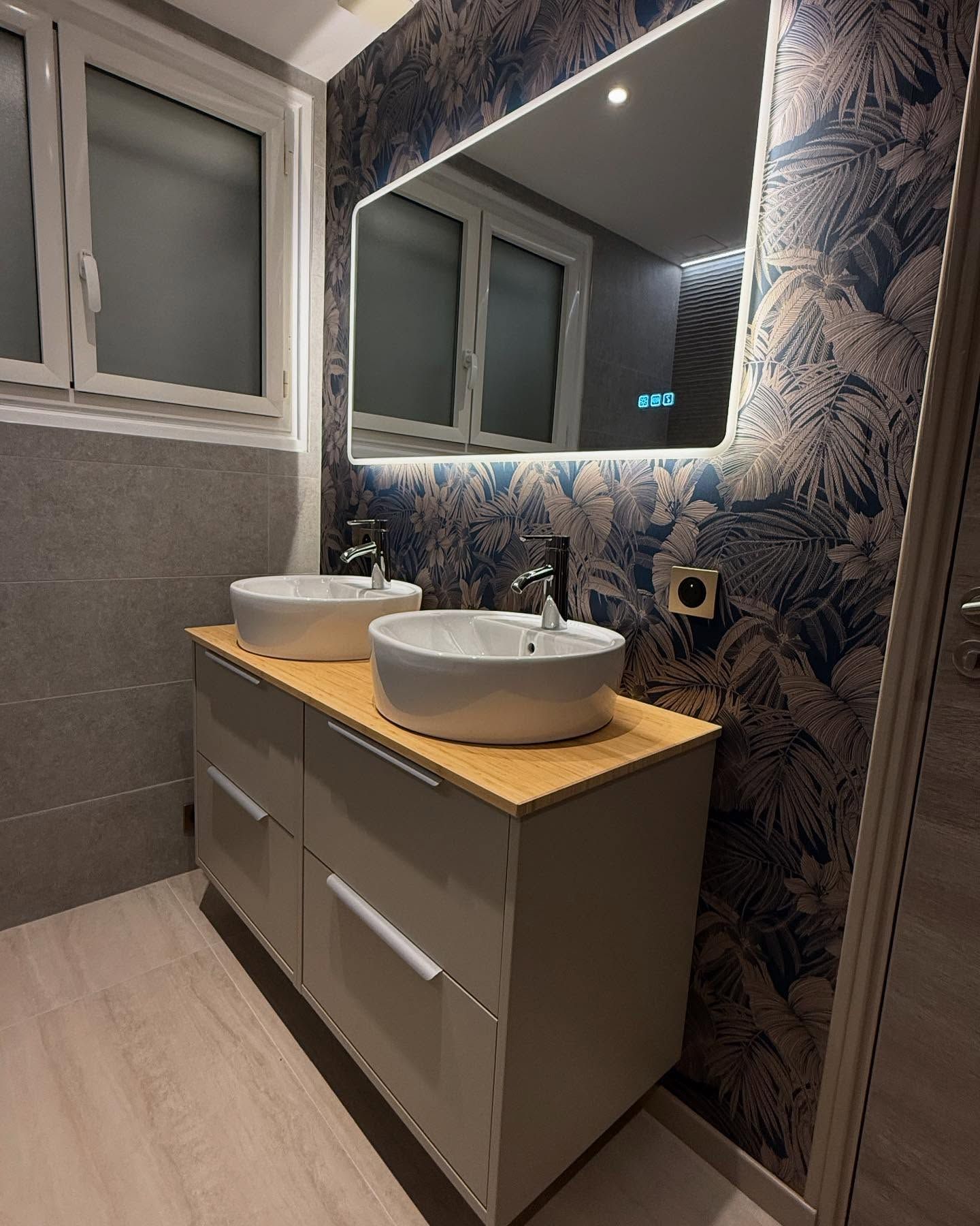 Salle de bains moderne avec double vasque, grand miroir et mur d'accent bleu à motifs.
