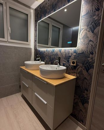 Salle de bains moderne avec double vasque, grand miroir et mur d'accent bleu à motifs.