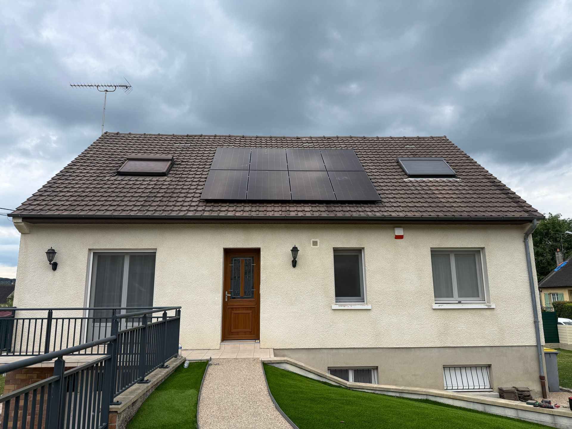 Maison avec panneaux solaires sur le toit sous un ciel nuageux, vue depuis l'allée d'entrée.