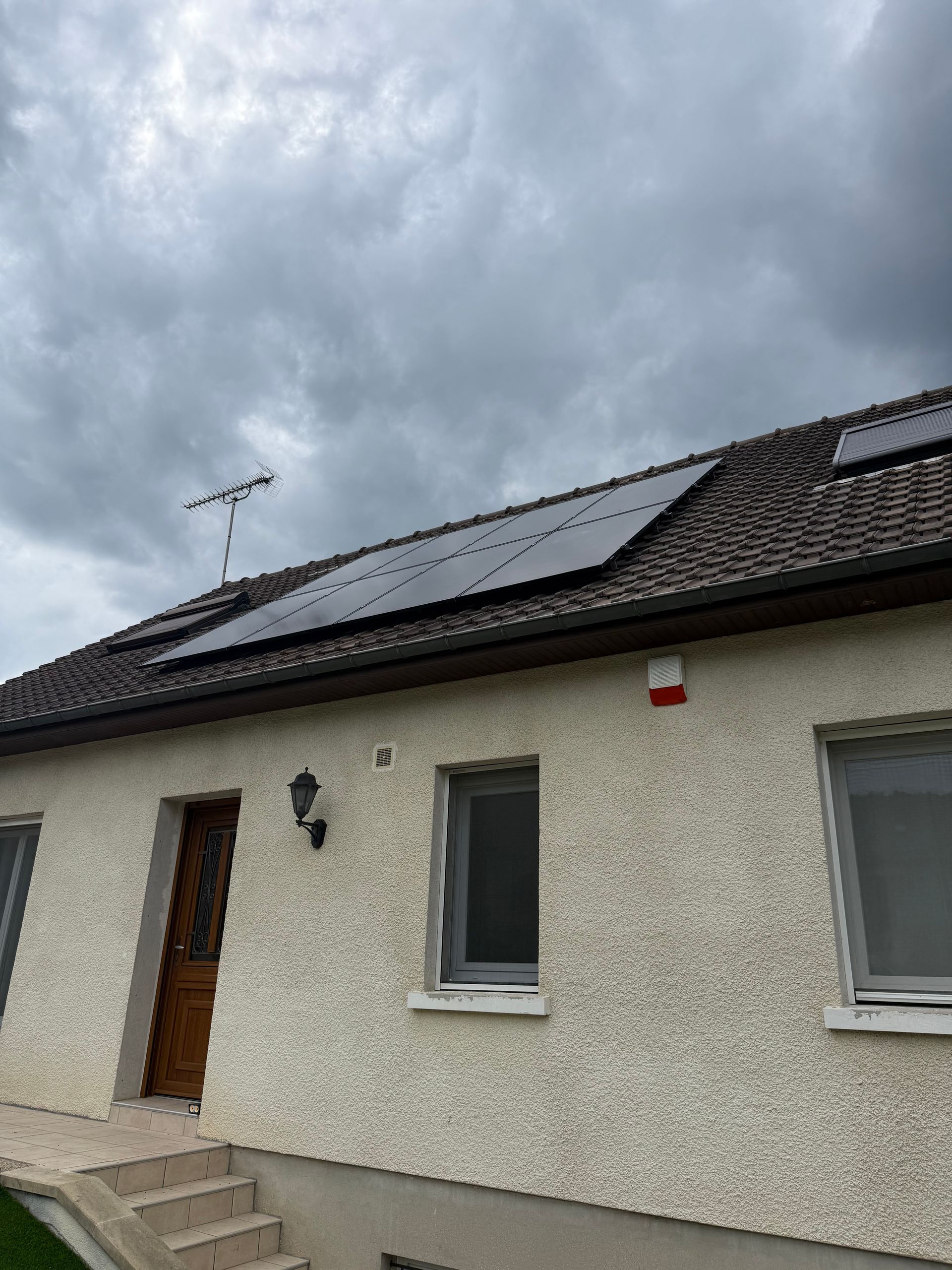 Toit de maison avec panneaux solaires sous un ciel nuageux.