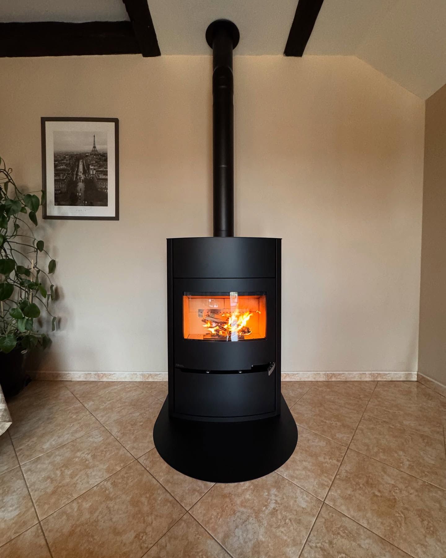 Poêle à bois noir moderne avec un feu vif dans une pièce carrelée, contre un mur beige.