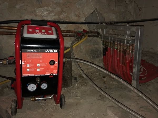 Machine de désembouage rouge dans un atelier poussiéreux, à côté de tuyaux et de colliers de serrage sur un support mural.