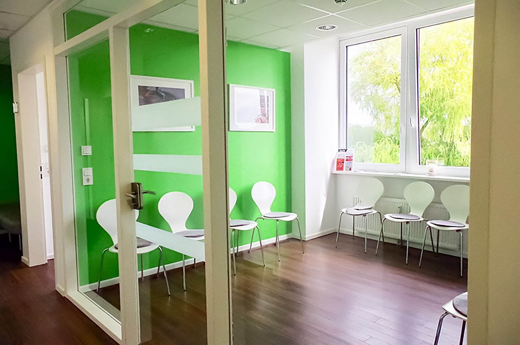 Ein Wartezimmer mit grünen Wänden und weißen Stühlen.