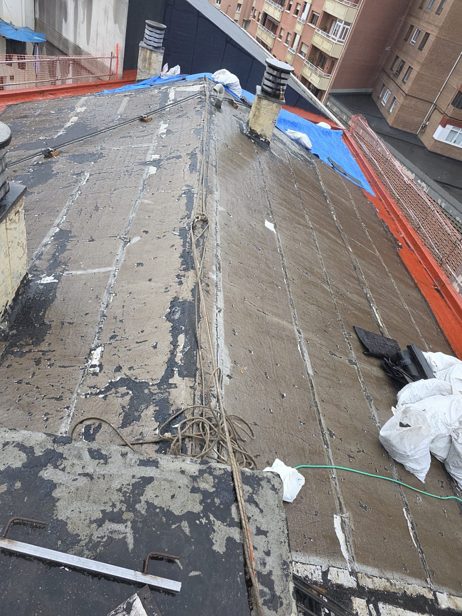 Un tejado inclinado en construcción, con la capa impermeabilizante a la vista, una chimenea y un borde de remate de color naranja brillante.