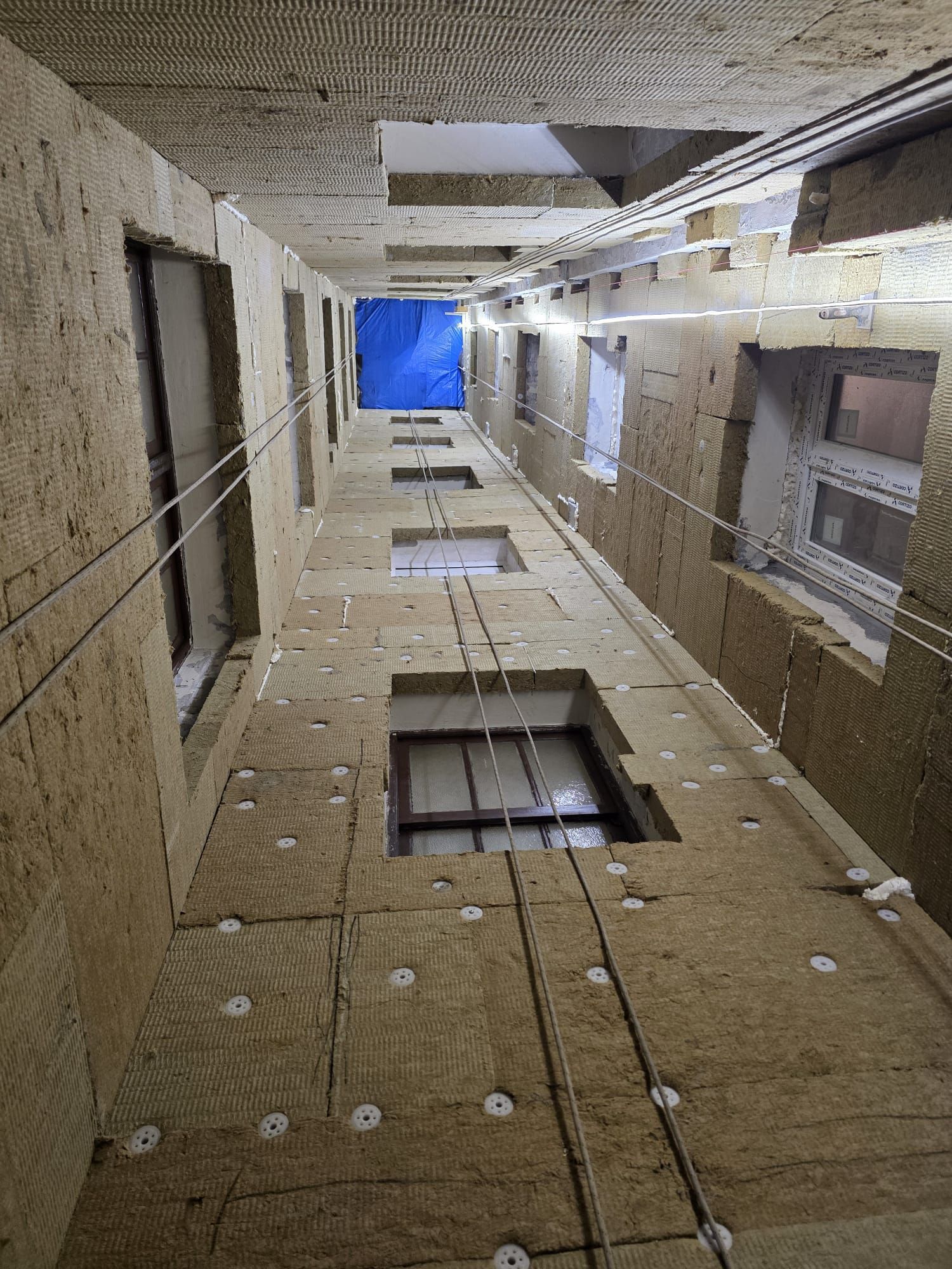 Un pasillo estrecho y sin terminar, en construcción, con paredes y techos cubiertos de paneles aislantes de color beige.