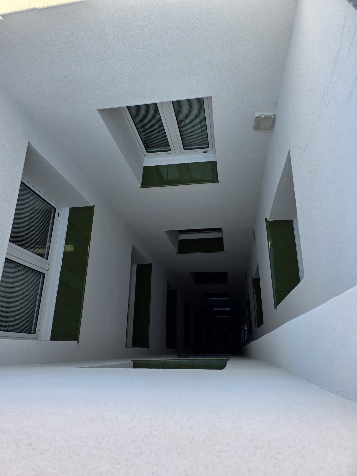 Vista desde un ángulo bajo de un largo pasillo interior minimalista de color blanco, con tragaluces empotrados y ventanas a lo largo de las paredes.