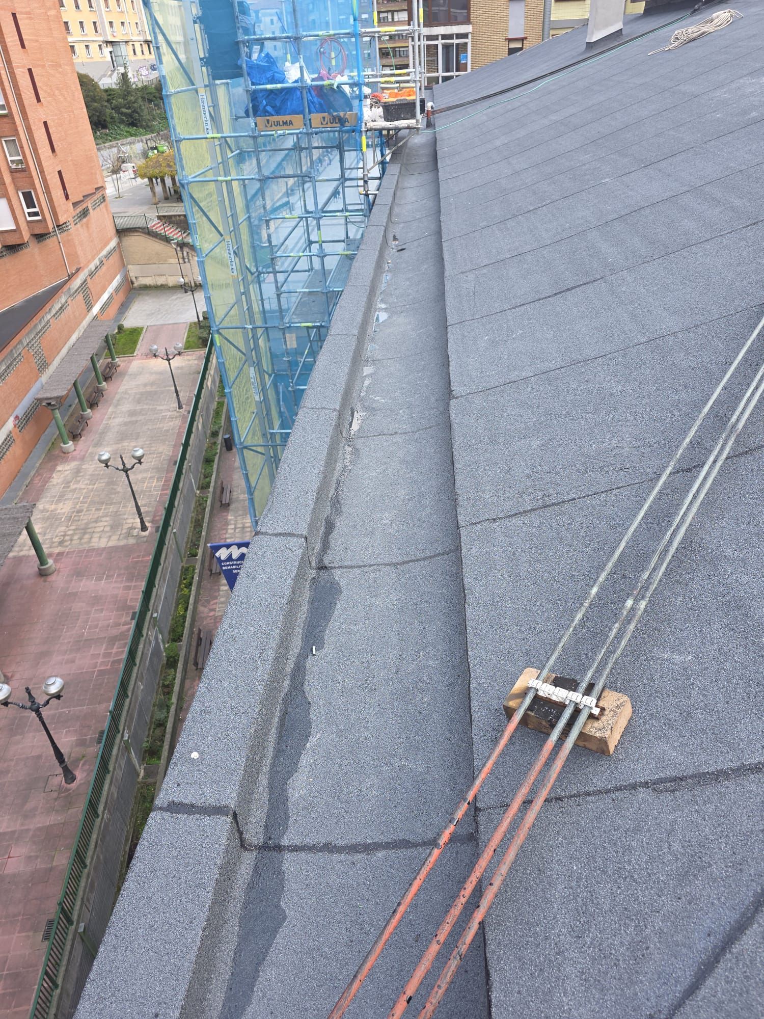 Vista desde un tejado gris a dos aguas hacia una calle con andamios y pararrayos instalados en las tejas.