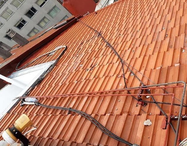 Vista desde una azotea con tejas naranjas, donde se aprecian cables eléctricos y tuberías a la vista, así como una estructura de tragaluz blanca.