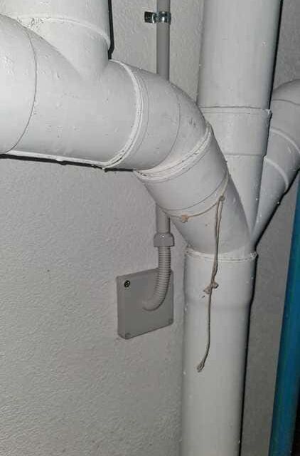 Tuberías de plástico blanco conectadas en una unión contra una pared blanca, con un trozo de cuerda colgando.