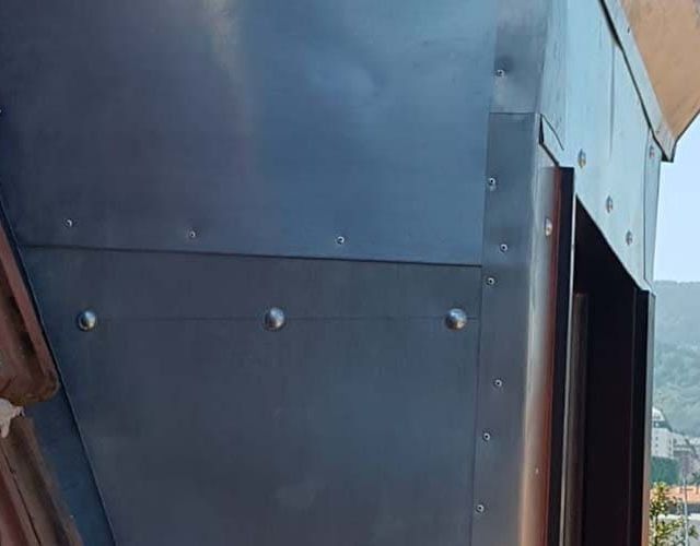 Primer plano de un revestimiento de techo metálico color carbón con remaches visibles y juntas limpias en un día despejado.