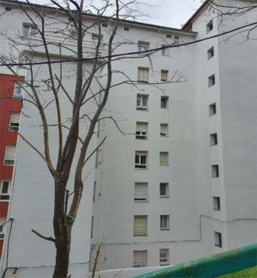 Un árbol de ramas desnudas se alza frente a un edificio de apartamentos blanco de varias plantas, con una sección roja a la izquierda.