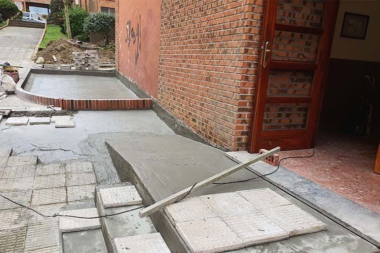 Obra en construcción en el exterior de un edificio, donde se aprecian rampas y escalones de hormigón fresco que se están formando con tablones de madera.