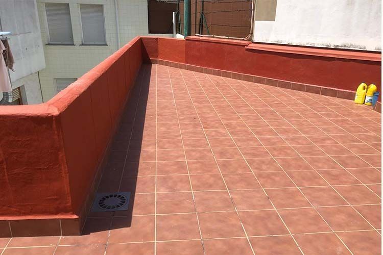 Una terraza exterior en la azotea con baldosas de terracota de color marrón rojizo, muros bajos a juego y un desagüe circular negro en el suelo.