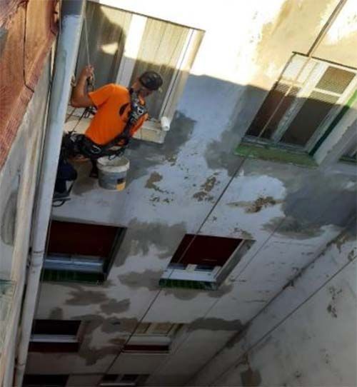 Una persona con una camiseta naranja desciende en rápel por el lateral de un edificio, pintando la fachada.