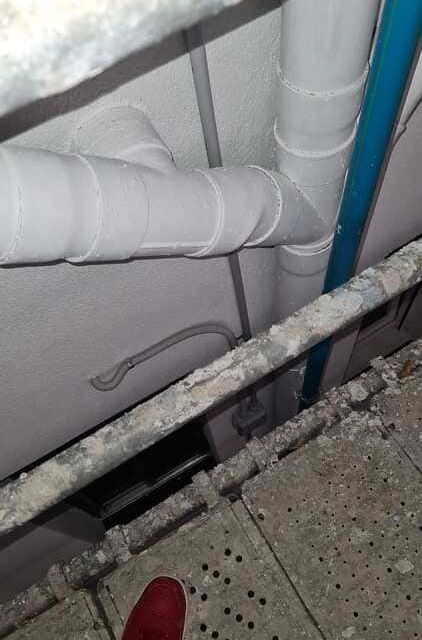 Tuberías blancas conectadas mediante una conexión en forma de Y en una pared de color claro, vistas desde una plataforma de construcción.