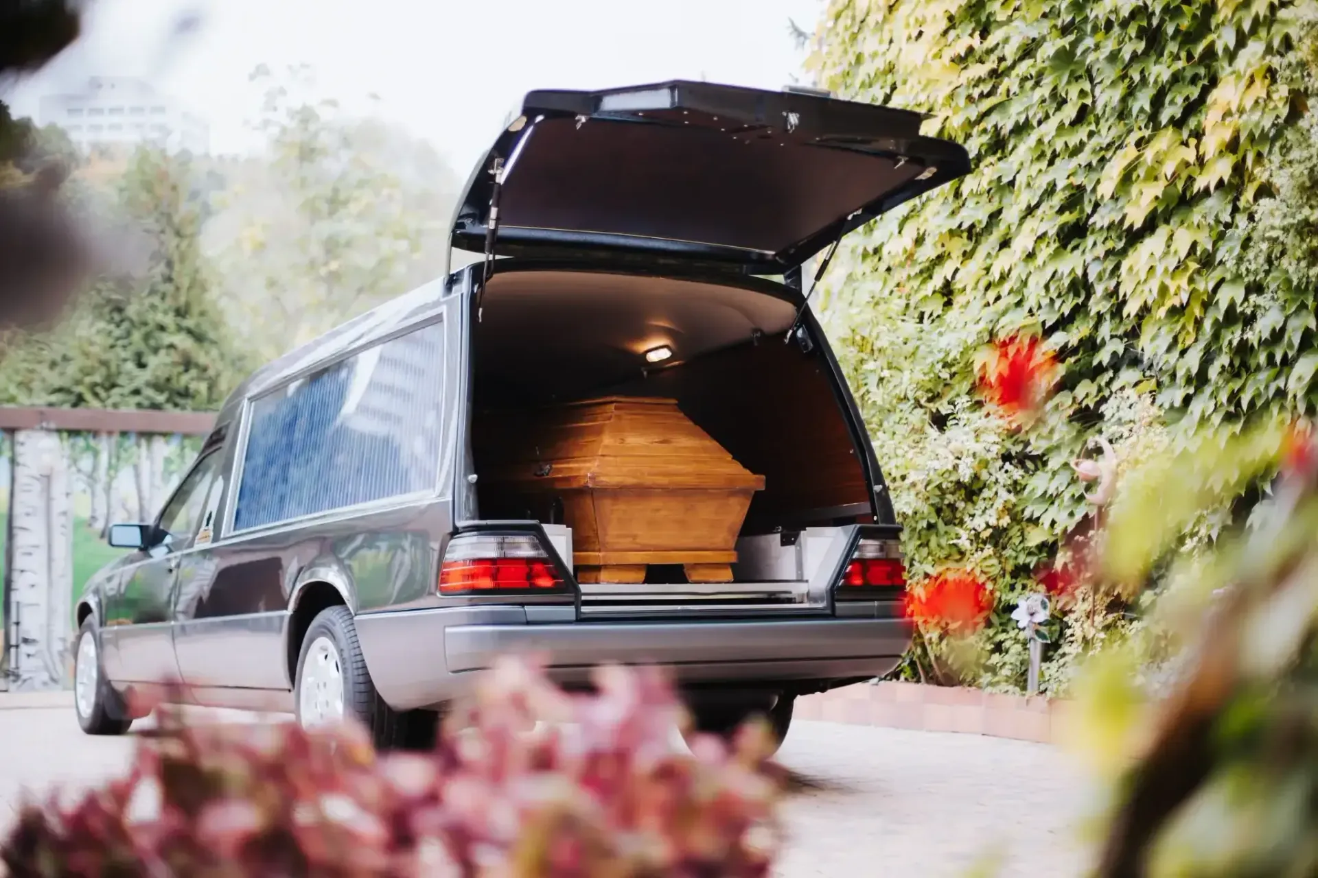 Coche fúnebre con la puerta trasera abierta, sosteniendo un ataúd, estacionado en un camino.