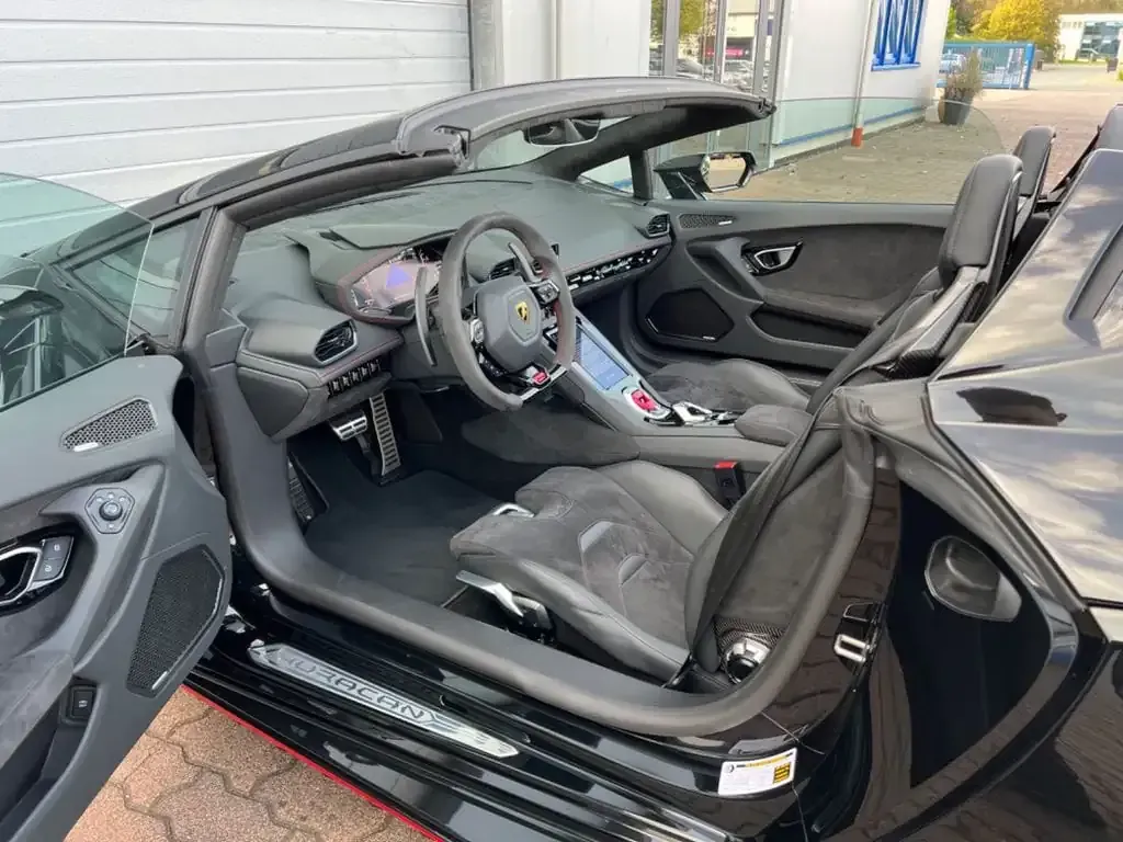 Interior convertible Lamborghini Huracan Spyder negro con puerta abierta, asientos grises y tablero negro.