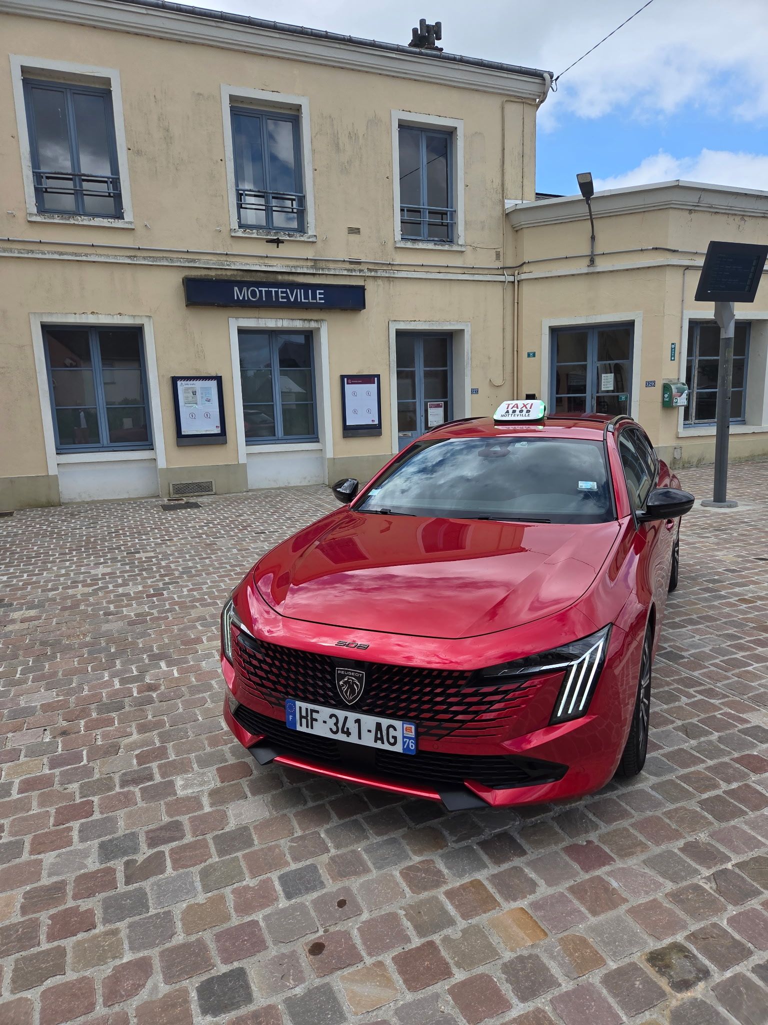 Voiture rouge avec le signe taxi, garée devant une gare.