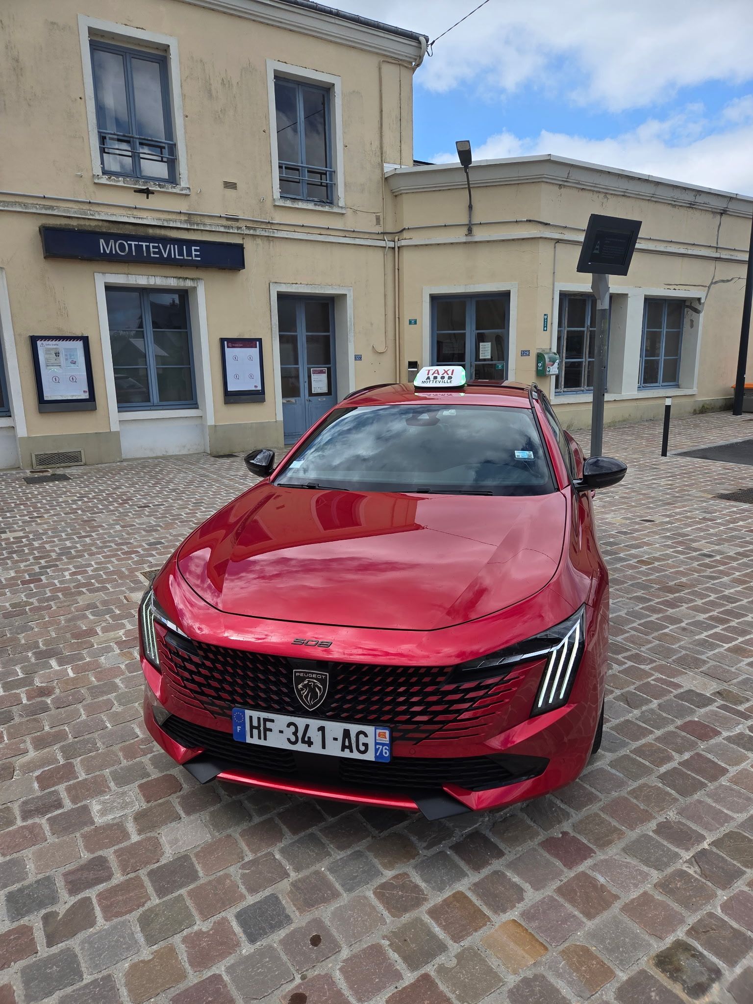 Taxi rouge dans une rue pavée devant la gare sous un ciel nuageux