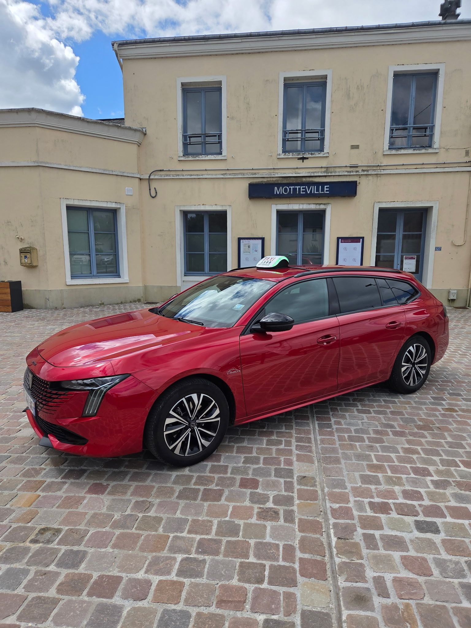 Une voiture rouge garée devant le parc de stationnement d'une gare.