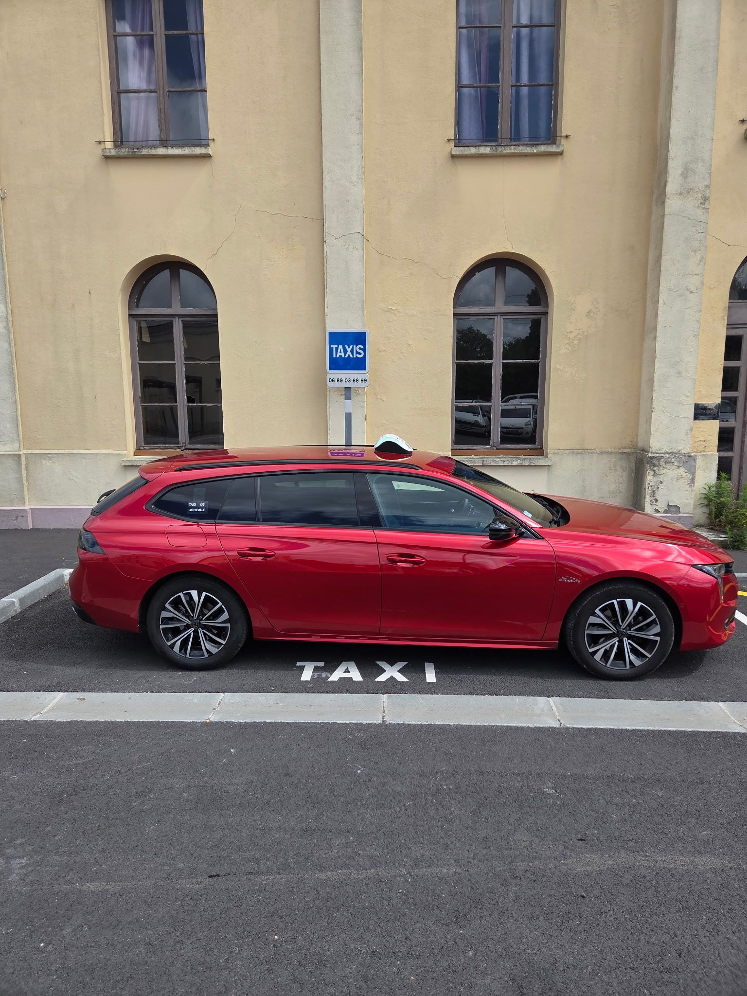 Un taxi 4x4 rouge est stationné à un emplacement réservé, à côté d'un bâtiment beige.