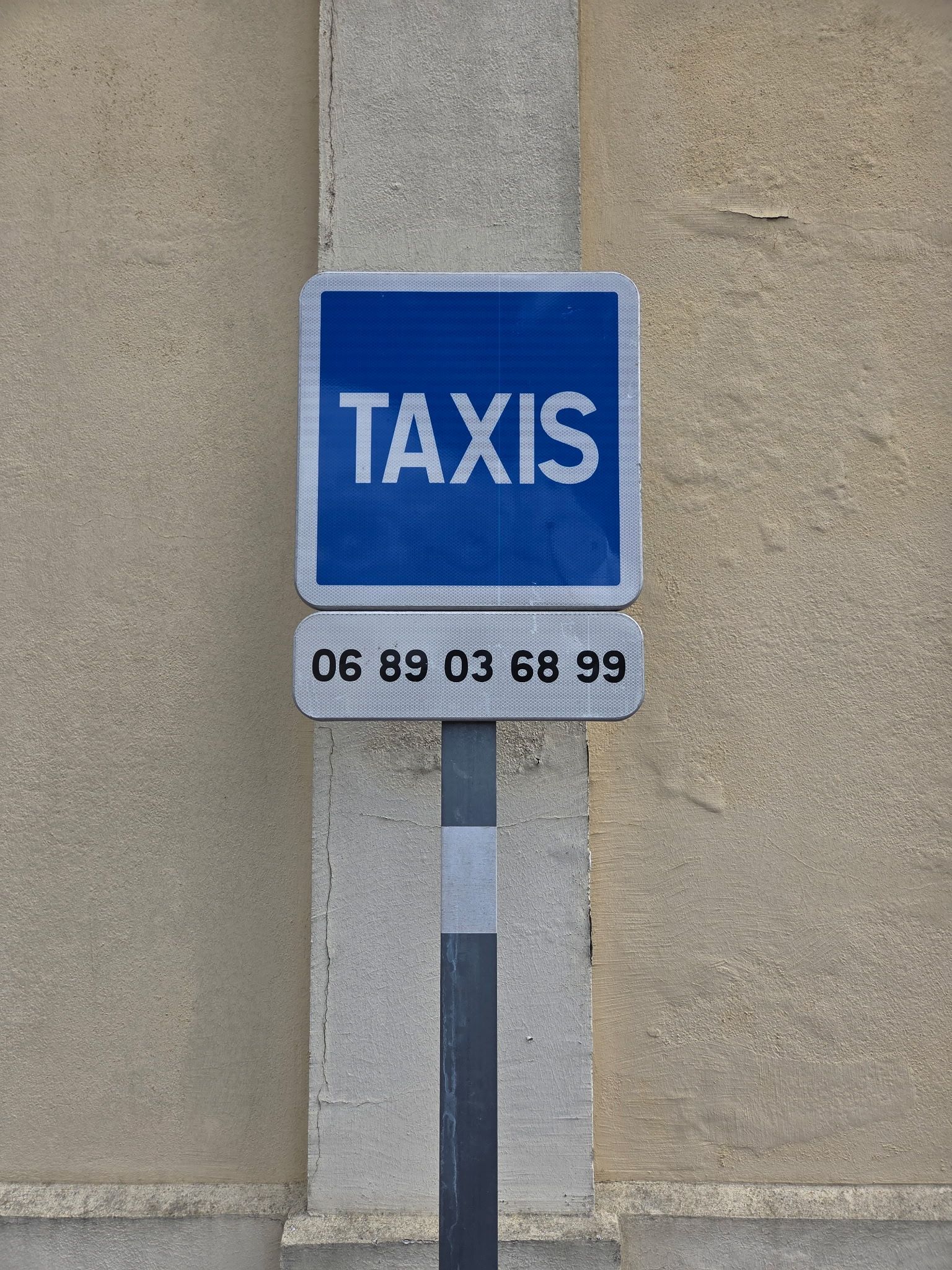 Panneau bleu de taxi sur un mur de pierre avec un numéro de téléphone en dessous.