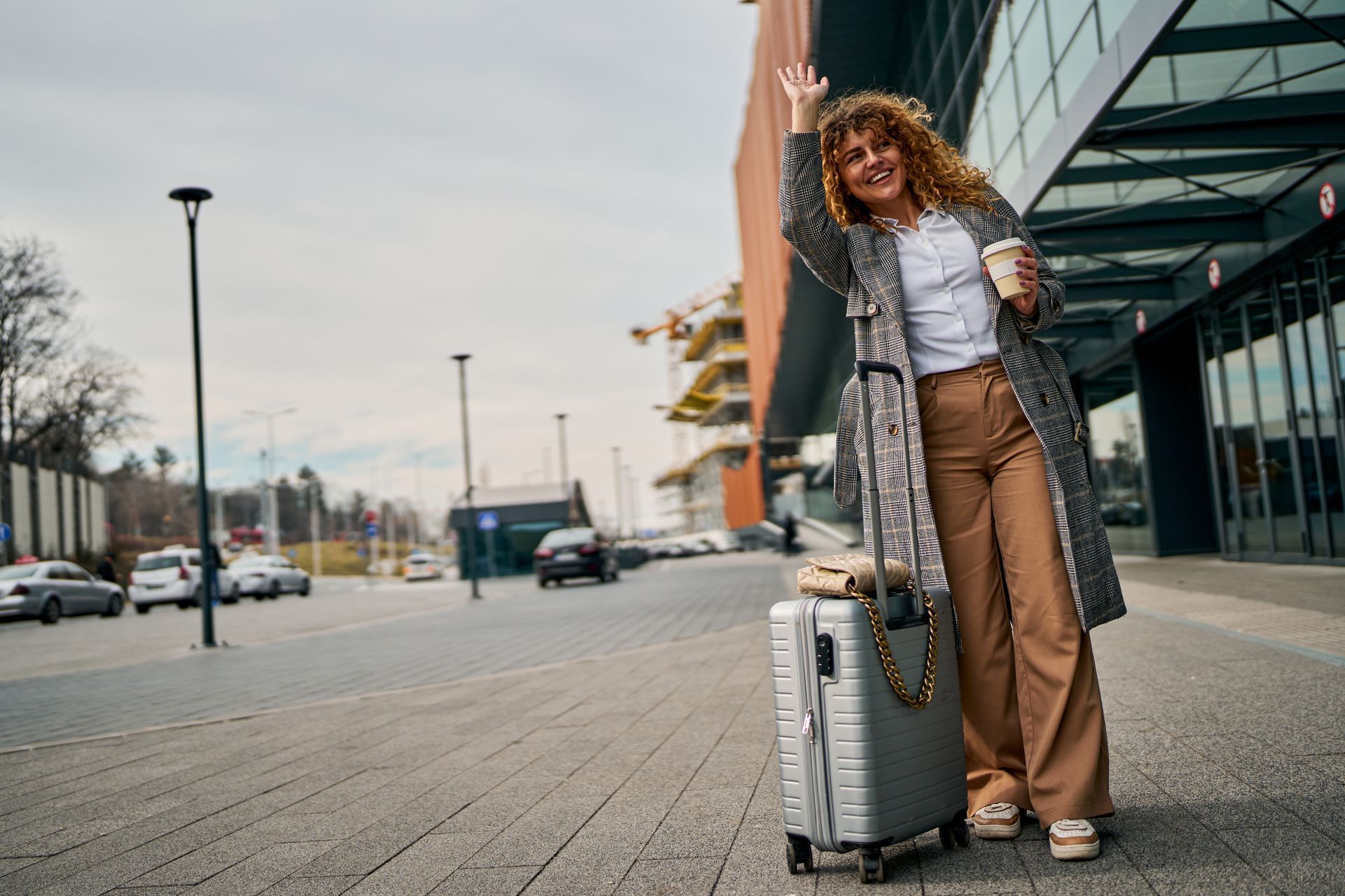 Voyageur faisant signe de la main à côté d'une valise devant un immeuble moderne dans une rue.