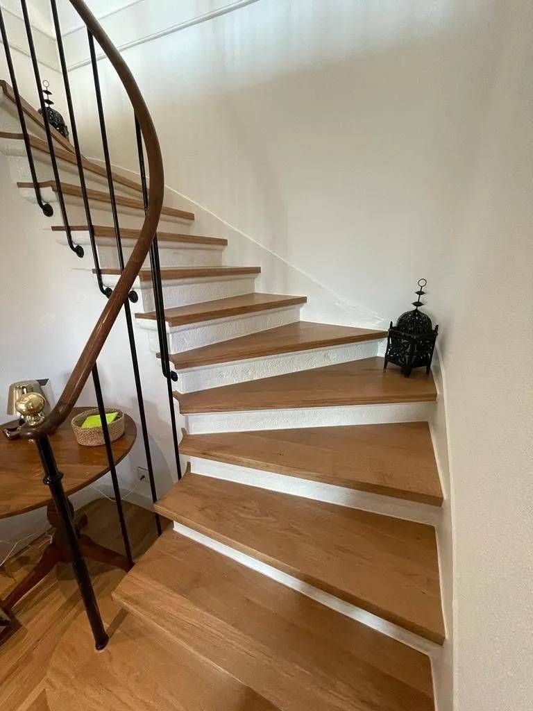 Escalier en bois avec marches blanches et rampe noire dans un couloir intérieur lumineux