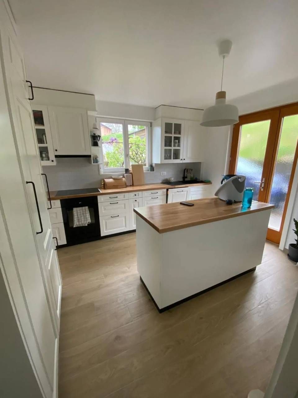 Cuisine moderne et lumineuse avec armoires blanches, îlot en bois et portes vitrées donnant sur une terrasse