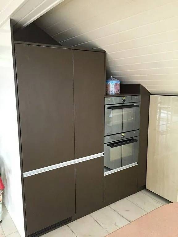 Cuisine compacte avec placards brun foncé, four encastré et plafond blanc incliné.