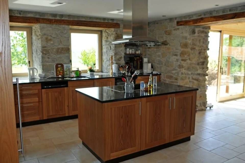 Cuisine en pierre et en bois avec un îlot central, un plan de travail noir et de grandes fenêtres.