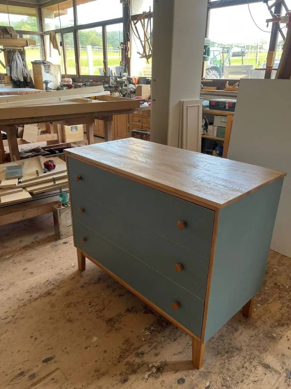 Commode bleue à trois tiroirs dans un atelier avec des établis en bois et de grandes fenêtres