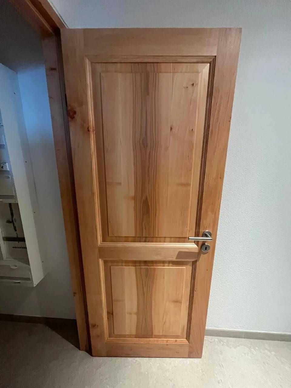 Porte intérieure en bois avec poignée argentée dans un couloir, encadrée de moulures en bois et de murs blancs.