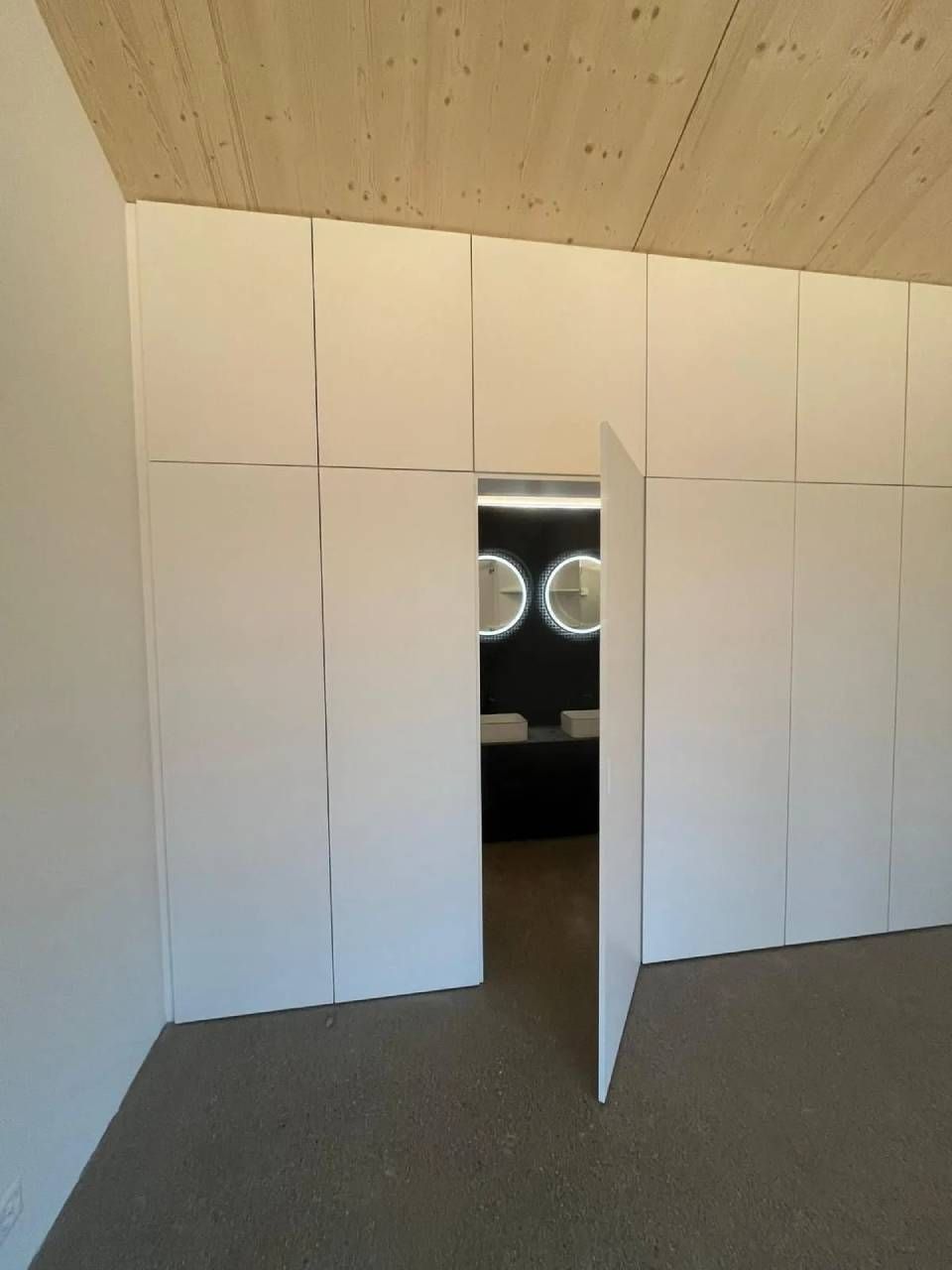 Pièce lambrissée blanche avec une porte étroite et ouverte et deux lumières rondes visibles dans la pièce du fond