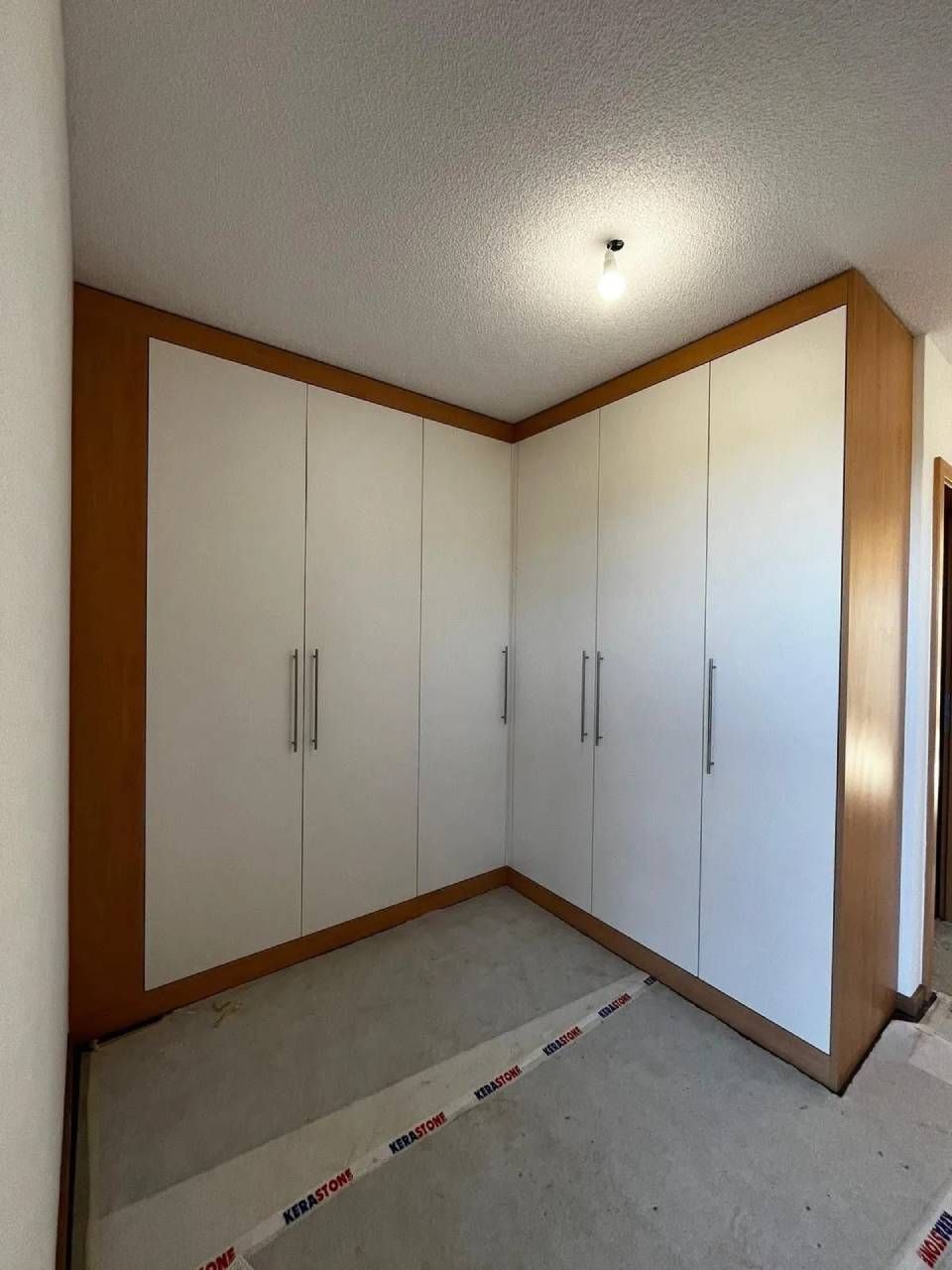 Portes de placard blanches intégrées dans une pièce d'angle recouverte de moquette, avec des boiseries et un plafonnier.