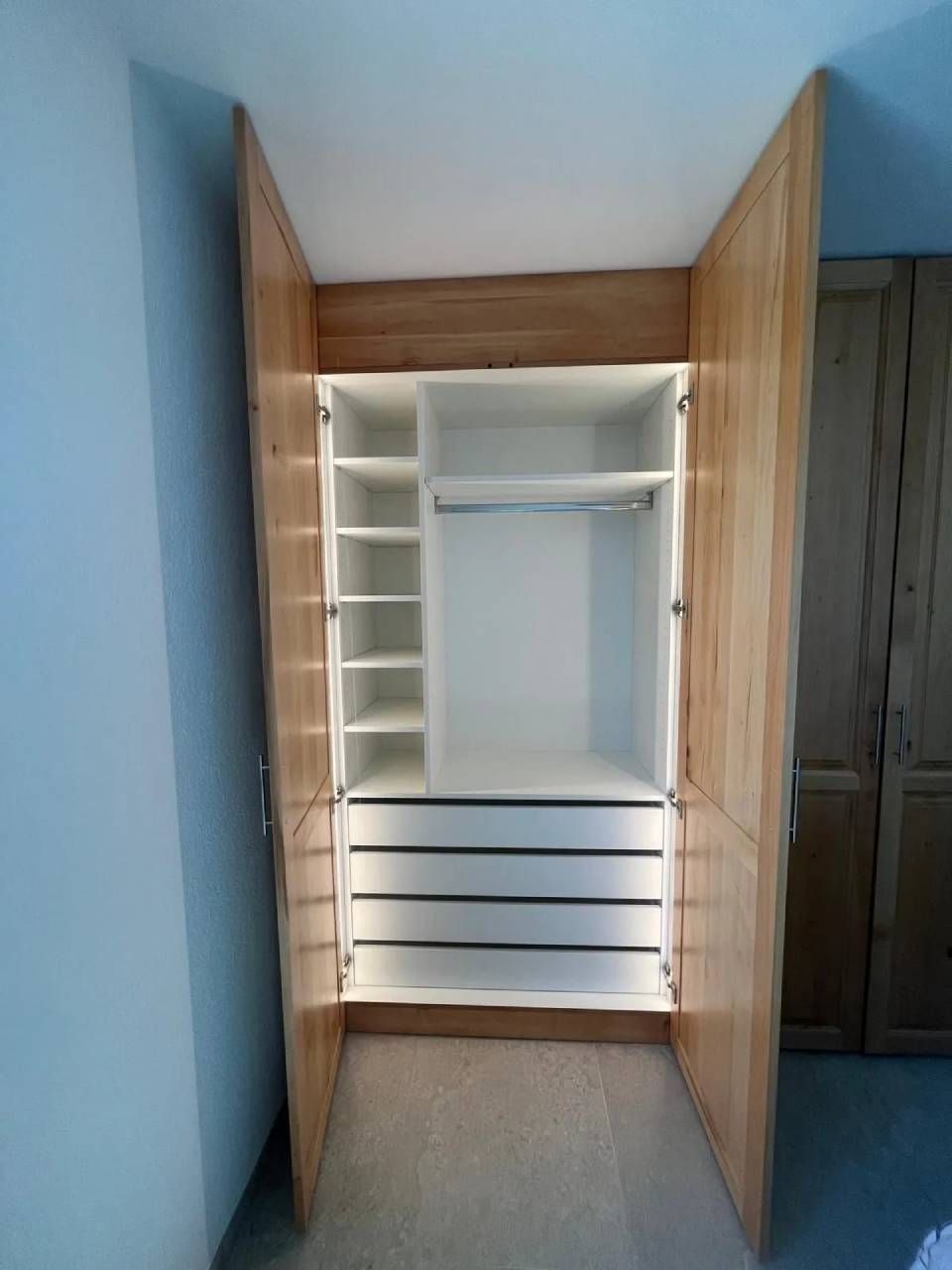 Armoire ouverte avec étagères, tiroirs et penderie dans une pièce aux murs bleus.