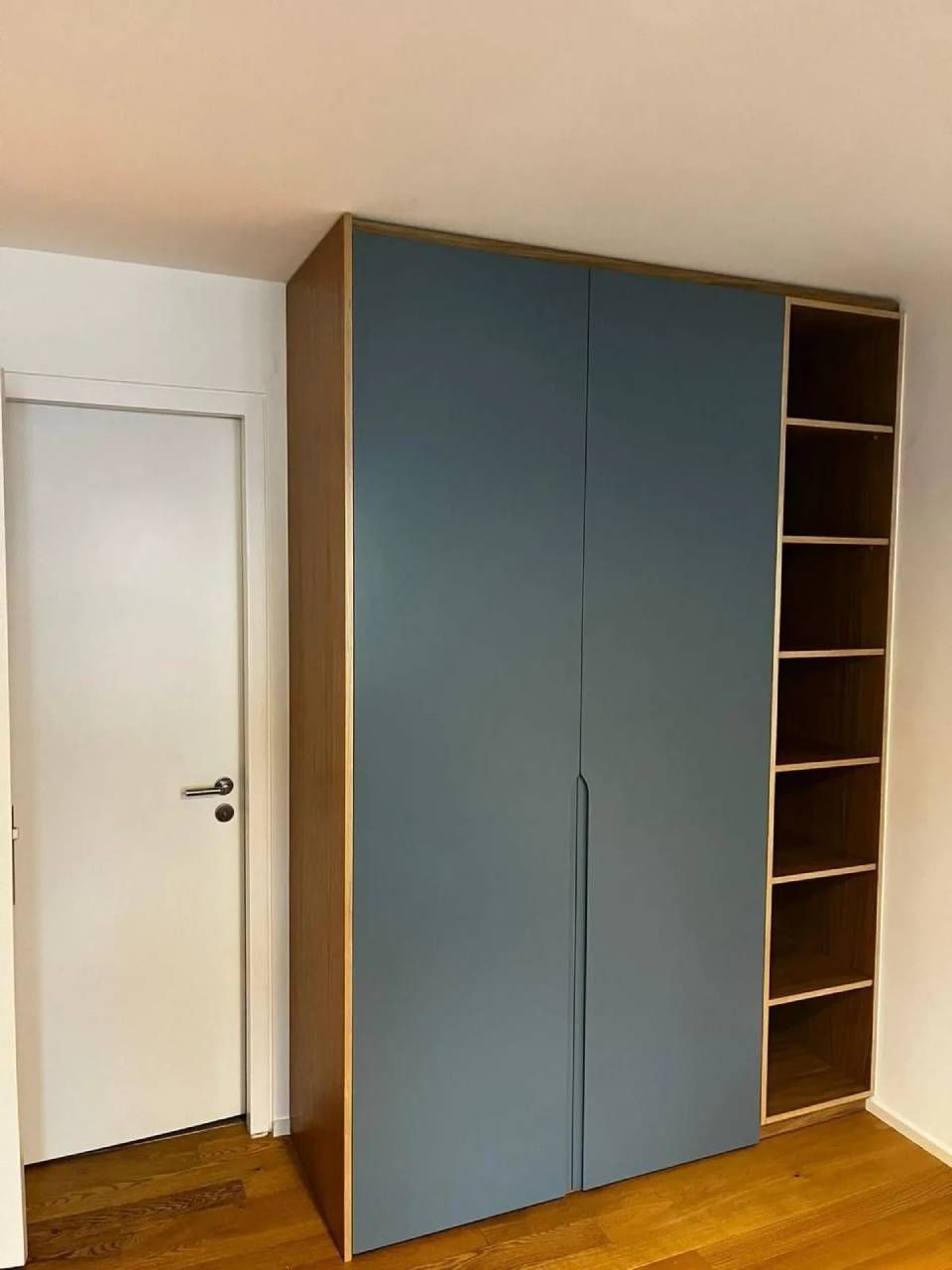 Une armoire bleue à étagères ouvertes se trouve à côté d'une porte blanche dans une pièce.