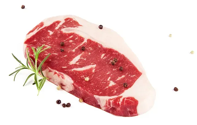 Un trozo de filete crudo con pimienta y romero sobre un fondo blanco.