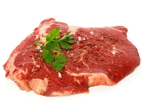 Un trozo de carne cruda con perejil y sal sobre un fondo blanco.