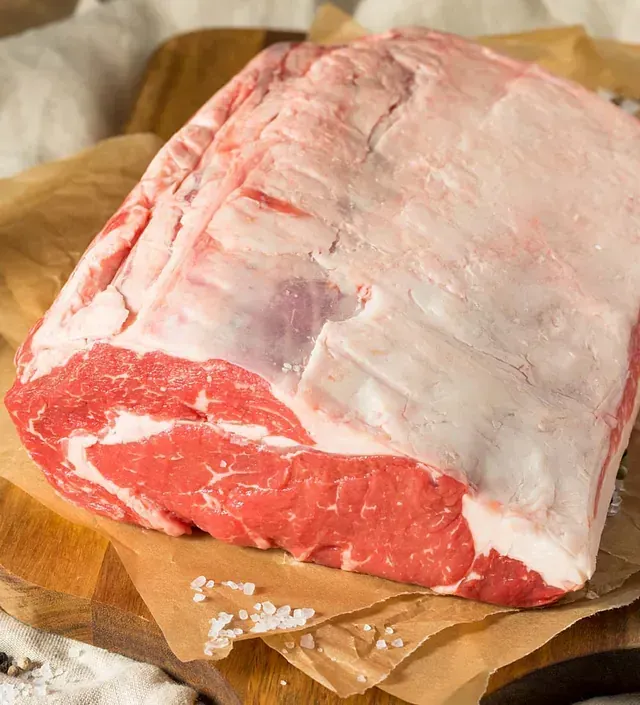 Un trozo de carne cruda reposa sobre un trozo de papel sobre una tabla de cortar de madera.