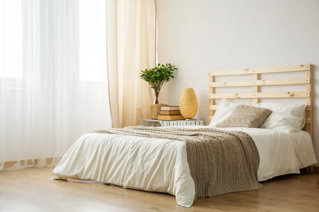 Dormitorio con cama, cabecero de madera, cortinas ligeras y suelo de madera.