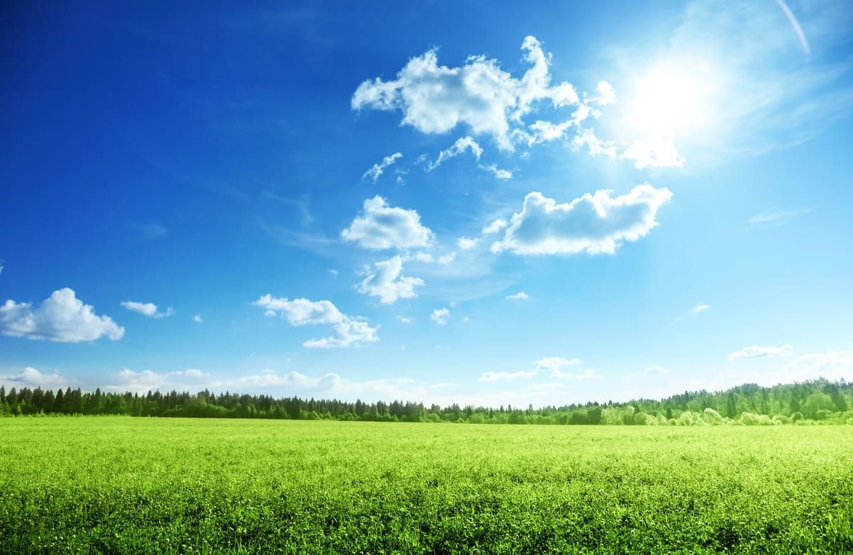El sol brilla a través de las nubes sobre un campo verde.