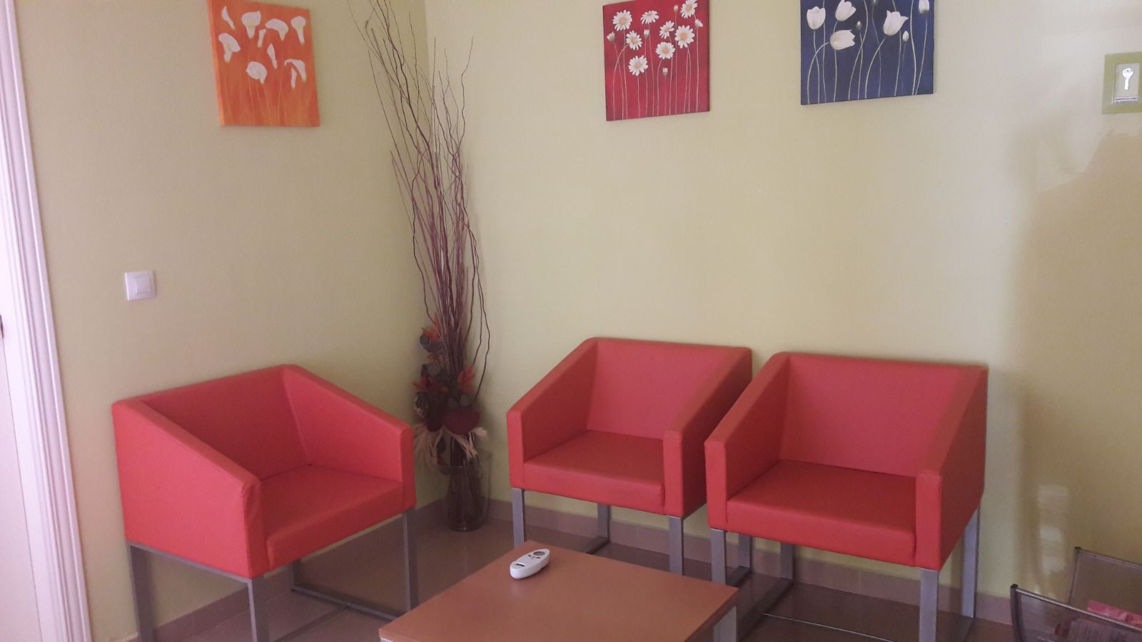 Una sala de espera con tres sillas rojas y una mesa de café.