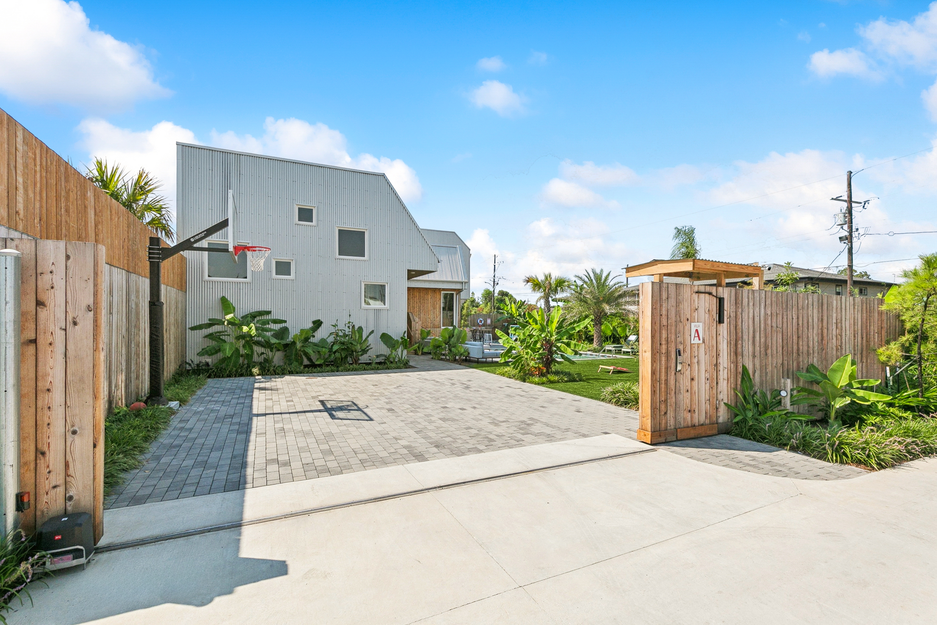 Modern house with light wood fence, basketball hoop, and paved driveway under a blue sky.