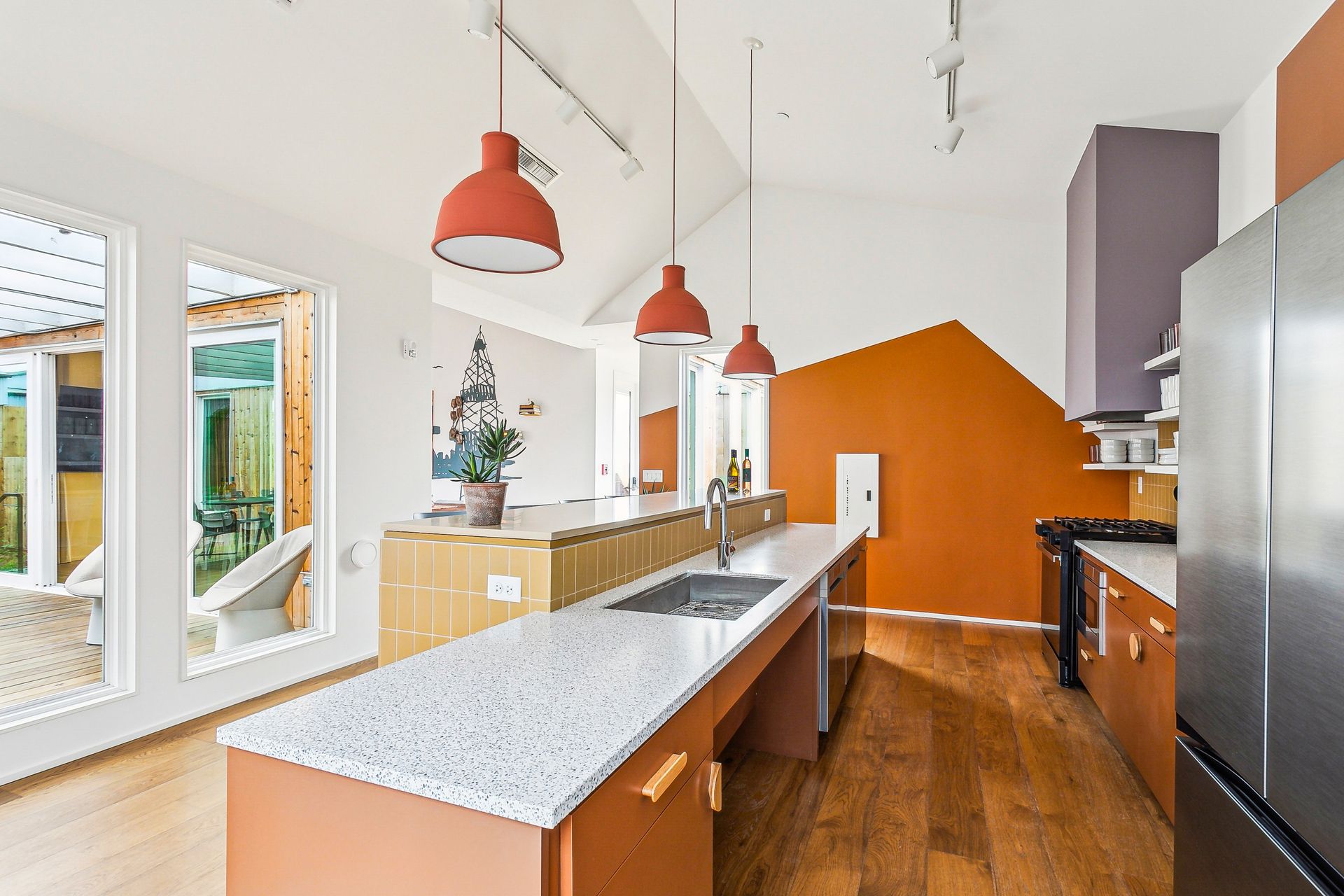 Modern kitchen with orange accents, white countertops, and wooden floors; view of the island and appliances.