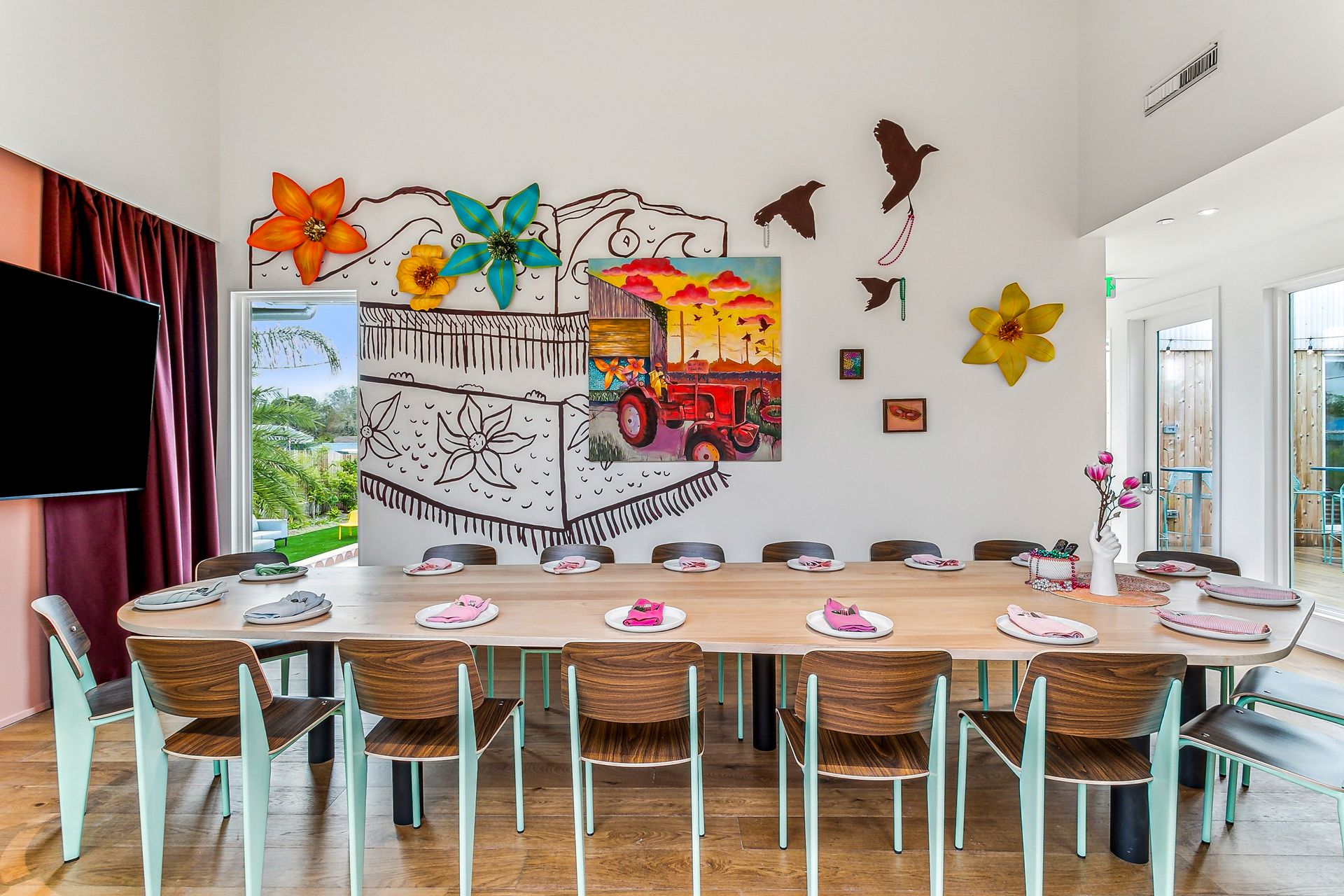Long dining table in a bright room, decorated with colorful art and flowers.