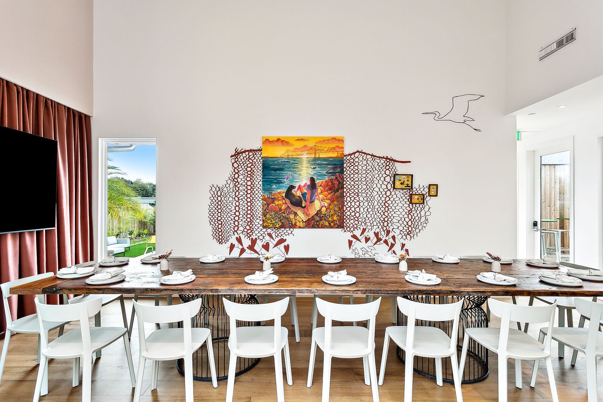 Long dining table with white chairs. Art on wall, window with lake view.