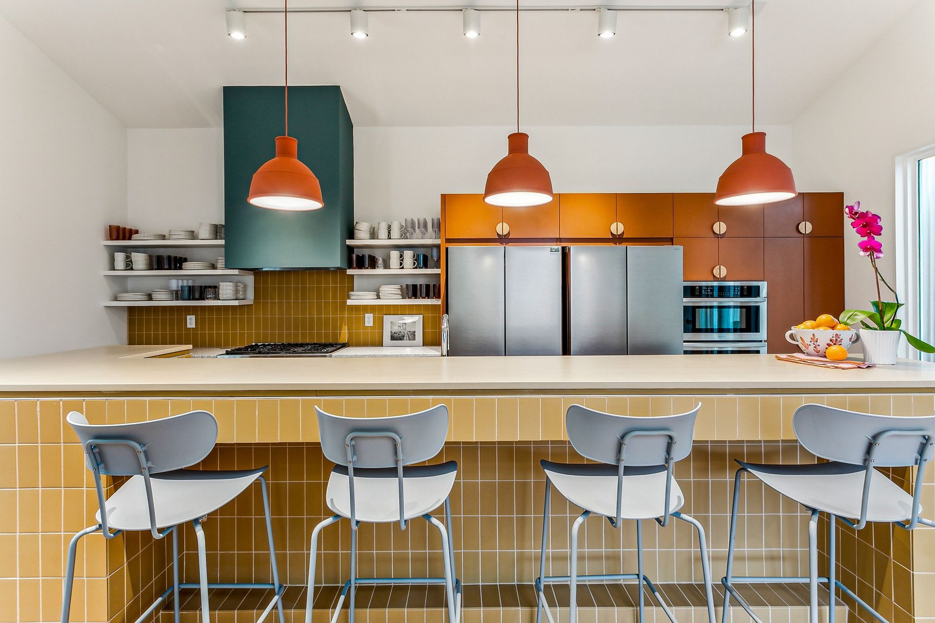Modern kitchen with orange pendant lights, stainless steel appliances, and yellow tile.