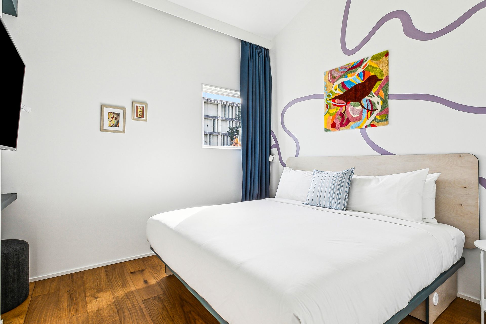 Bedroom with king bed, art, window, TV, and purple wall design.
