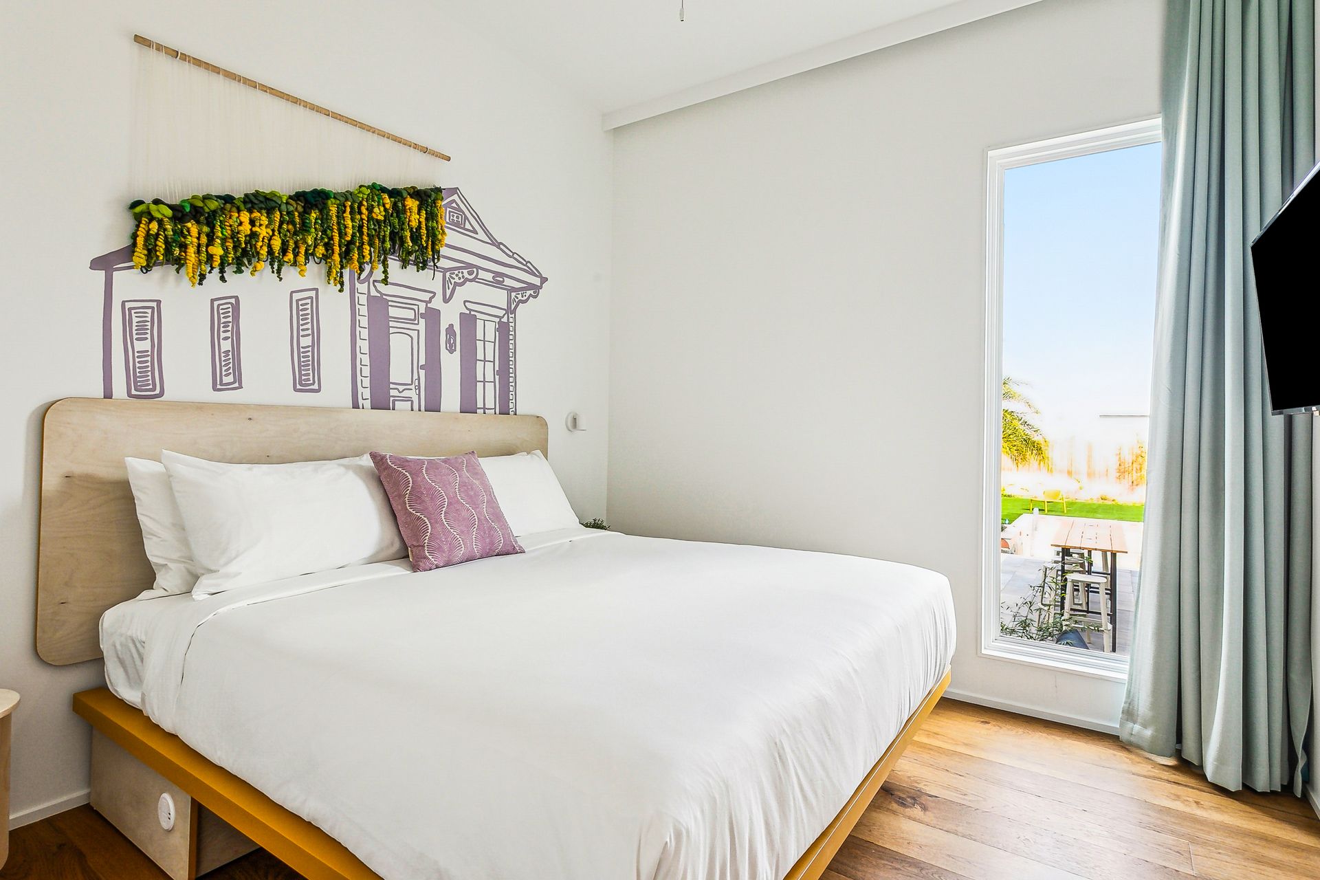 Bedroom with white bedding, floral artwork, and a large window overlooking a patio.